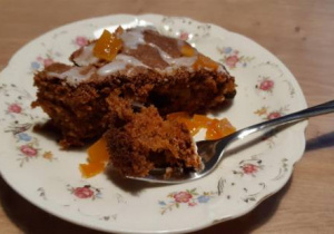 Kawałek ciasta marchewkowego z widelcem na talerzyku deserowym.